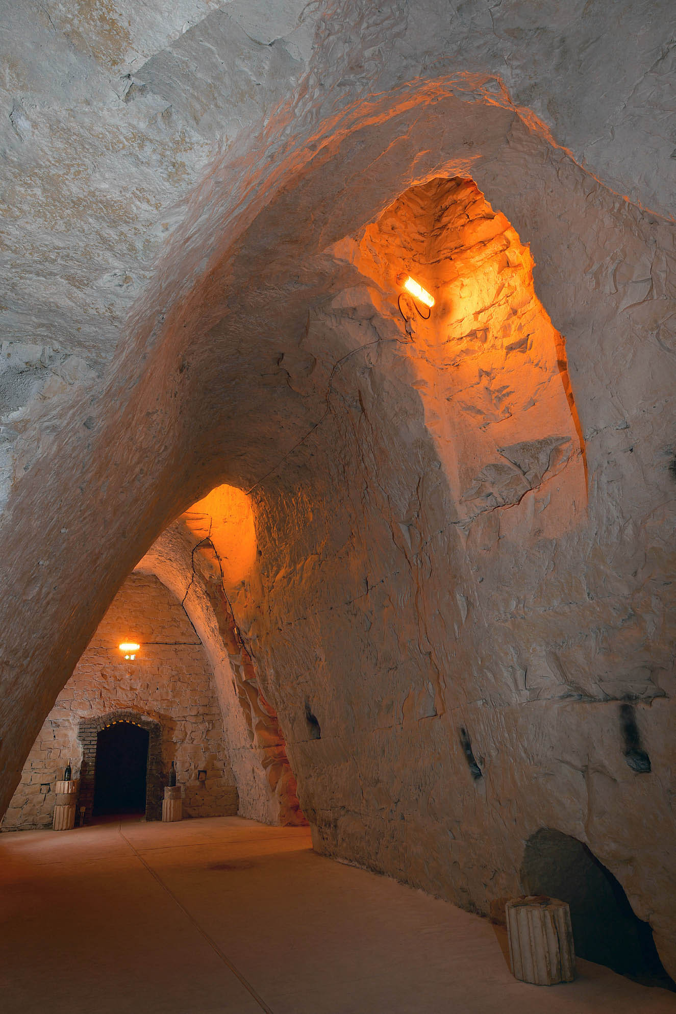 Corridor in the Crayères, the ceiling is vaulted, golden lights are hanging on the walls